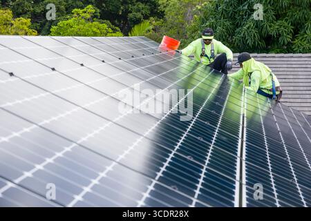 Männer mit Sicherheitsgurten, die auf dem Dach stehen und das LG NeonR installieren DC-Photovoltaikpaneele auf Aluminiumschienen bei einer Wohnphotovoltaik Installieren Stockfoto