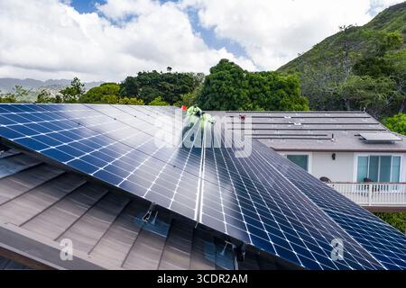 Männer mit Sicherheitsgurten, die auf dem Dach stehen und das LG NeonR installieren DC-Photovoltaikpaneele auf Aluminiumschienen bei einer Wohnphotovoltaik Installieren Stockfoto