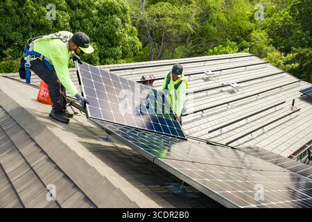 Zwei Männer arbeiten zusammen, um Photovoltaik-Paneele auf Aluminiumschienen auf dem Wohndach, Honolulu, Oahu, Hawaii, USA, zu installieren Stockfoto
