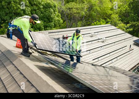 Zwei Männer arbeiten zusammen, um Photovoltaik-Paneele auf Aluminiumschienen auf dem Wohndach, Honolulu, Oahu, Hawaii, USA, zu installieren Stockfoto