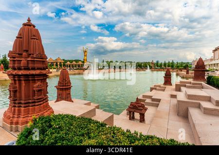 Robbinsville, NJ - USA - 2. August 2025 Goldene Statue von Neelkanth Varni erhebt sich über einem ruhigen See mit Springbrunnen, umgeben von kunstvollen Schnitzereien und üppigem Grün Stockfoto