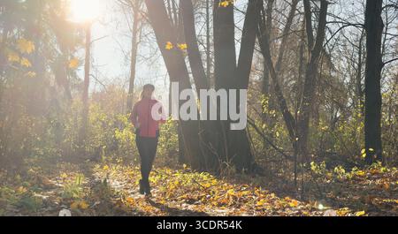 Waldweg im Herbst. Herbstläuferin, die in wunderschönen Laubwäldern läuft, Natur Hintergrund. Asiatische glückliche Sportfrau, die im Freien trainiert. Stockfoto