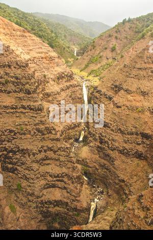 Der mehrstöckige Wasserfall zieht sich durch den roten Felsen des Waimea Canyon, der oft als Grand Canyon des Pazifiks bezeichnet wird. Stockfoto