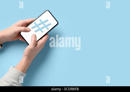Hände, die das Mobiltelefon halten, mit einem Hashtag-Zeichen auf dem Bildschirm vor blauem Hintergrund Stockfoto