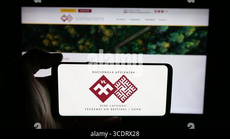 Deutschland. Juli 2025. In dieser Fotoabbildung hält eine Person ein Handy mit dem Logo der lettischen Partei Nacionala Apvieniba (NA) auf dem Bildschirm vor der Webseite. (Foto von Timon Schneider/SOPA Images/SIPA USA) *** ausschließlich für redaktionelle Nachrichten *** Credit: SIPA USA/Alamy Live News Stockfoto