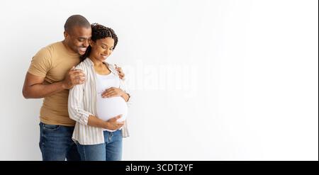 Liebevolles afroamerikanisches Paar, das zusammen steht, Mann, der schwangere Frau umschließt Stockfoto