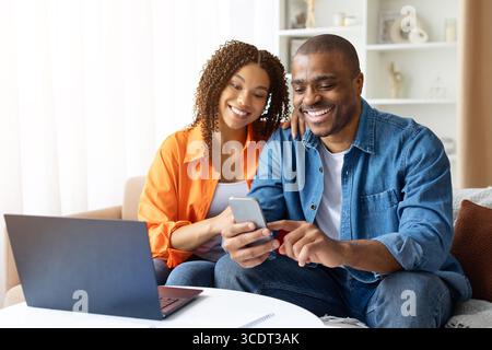Lächelndes afroamerikanisches Paar, das zu Hause ein Smartphone nutzt, App durchsucht Stockfoto