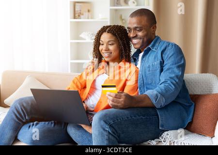 Schwarzes junges Paar online einkaufen mit Laptop und Kreditkarte zu Hause Stockfoto