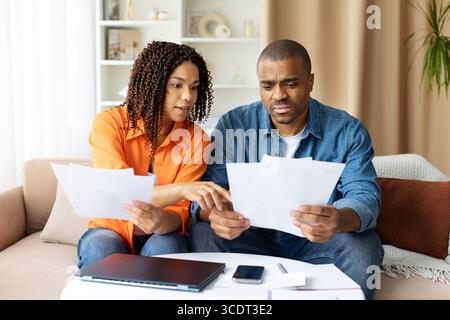 Ernsthaftes junges afroamerikanisches Paar, das Dokumente zu Hause zusammen überprüft Stockfoto