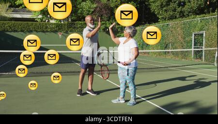 High-Five-Mann und ältere hispanische Frau in Tenniskleidung auf dem Tennisplatz mit Umschlag-Ikonen Stockfoto