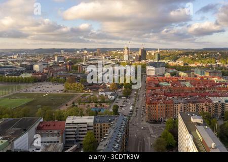 Aus der Vogelperspektive des goldenen Sonnenlichts, das die roten Dächer und Grünflächen einer pulsierenden Stadt küsst, enthüllt das Ullevi-Stadion und entfernte Wahrzeichen, Göteborg, Vastra Gotaland, Schweden. Stockfoto