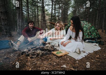Eine Gruppe von Freunden, die im Wald campen und gemeinsam eine Mahlzeit genießen Stockfoto