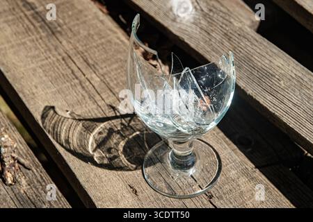 Zerbrochenes Weinglas mit zersplitterten Stücken auf einem Holztisch, vor einem unscharfen Hintergrund Stockfoto
