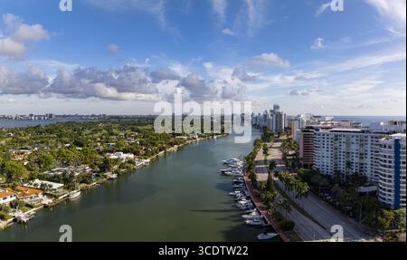 Aus der Vogelperspektive auf den Intracoastal Waterway, der den Himmel reflektiert, gegenüber den hoch aufragenden Gebäuden und dem üppigen Grün entlang der Collins Avenue, Miami B. Stockfoto