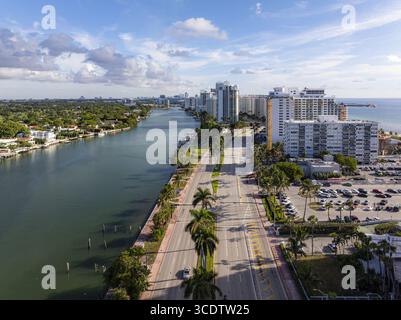 Blick aus der Vogelperspektive auf die Collins Avenue, flankiert von der noch immer intraküstennahen Wasserstraße und hoch aufragenden Strukturen unter einem Himmel mit Wolken, Miami Beach, blorid Stockfoto