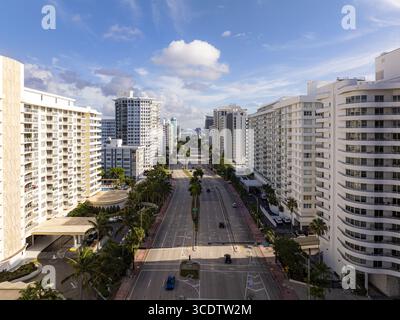 Blick aus der Vogelperspektive auf die Collins Avenue im Sonnenlicht, flankiert von hoch aufragenden weißen Gebäuden vor einem blauen Himmel mit Wolken, Miami Beach, Florida, Uni Stockfoto