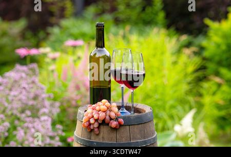 Zwei Gläser und eine Flasche Rotwein im grünen Garten auf Fass Stockfoto