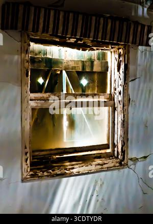 Ein altes Fenster mit abblätternder Farbe und einer gestreiften Markise. Das Fenster ist mit Holzdielen überdacht, und Licht scheint durch die Risse. Stockfoto
