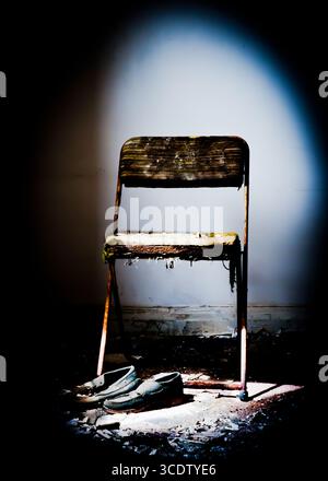 Ein alter Stuhl und ein Paar Schuhe werden von einem Scheinwerfer in einem dunklen Raum beleuchtet. Stockfoto