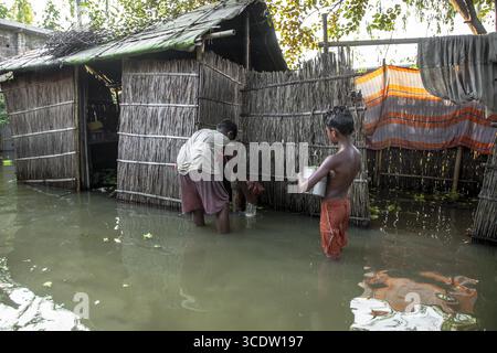 Kurigram, Bangladesch - 14. Juli 2024: Blick auf überflutete Häuser, in denen zwei Kinder im trüben Wasser stehen, ihre Widerstandsfähigkeit ist ein starker Kontrast zu den baufälligen Strukturen. Stockfoto