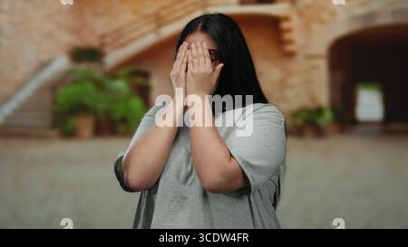 Die Frau, die im Freien in einer städtischen Straßenlage lächelt, zeigt Glück und Selbstvertrauen mit lässiger Kleidung und Brille, die einen charmanten Stil in Plus-Größe unterstreichen Stockfoto