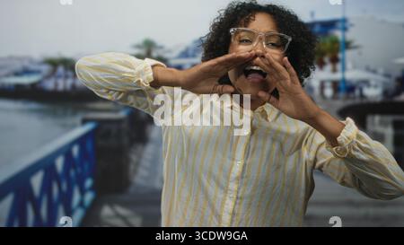 Frau mit tanzen erhobenen Händen auf der Straße in der Nähe des Fußwegs am Meer unter sanfter Morgensonne; Gelassenheit. Stockfoto