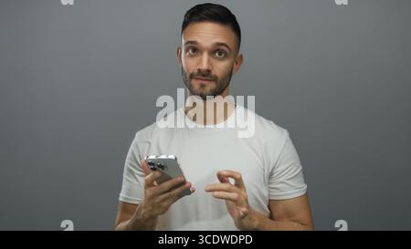 Junger Mann mit Smartphone mit fokussiertem Ausdruck vor grauem Hintergrund, der moderne Technologie und Kommunikation zeigt. Stockfoto