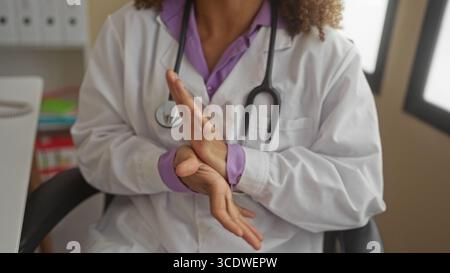 Hispanische Transgender-Ärztin mit Labormantel und Stethoskop, die im Klinikgebäude die Hände reibt; mitfühlende Pflege. Stockfoto