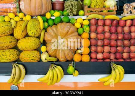 Farbenfrohe Ausstellung von Obst und Gemüse, einschließlich Äpfeln, Bananen, Orangen und Kürbissen. Die Kürbisse werden in die Mitte des Tisches gestellt, Surro Stockfoto