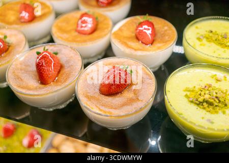 Reihe von Desserts mit Erdbeeren darauf. Einer der Desserts ist grün. Die Nachspeisen sind in Glasschalen Stockfoto