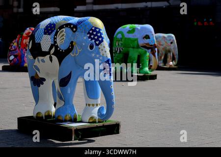 Gemalte Elefantenskulpturen in Beursplein, Amsterdam, Niederlande, auf Paletten bei Tageslicht, mit weiteren Figuren im Hintergrund. Stockfoto