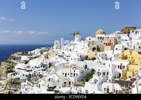 Weiße und bunt bemalte Ferienhäuser an einem steilen Hang, Windmühlen, Blick auf Oia, Thira, Santorini, Kykladen, Griechenland Stockfoto