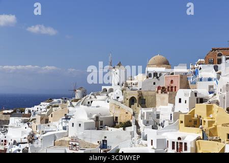 Weiße und bunt bemalte Ferienhäuser an einem steilen Hang, Windmühlen, Cumulus, Blick auf Oia, Thira, Santorini, Kykladen, Griechenland Stockfoto