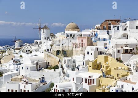 Weiße und bunt bemalte Ferienhäuser an einem steilen Hang, Windmühlen, Blick auf Oia, Thira, Santorini, Kykladen, Griechenland Stockfoto