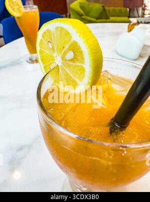 Ein großes Glas Eistee mit Zitronenscheiben und schwarzem Stroh auf einem Marmortisch in einer hellen Hotelbar in Dubai, VAE Stockfoto