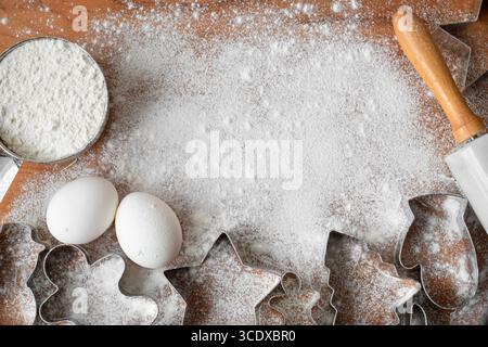 Blick von oben auf das Backen von weihnachtskeksen mit Ausstechern, Eiern, Mehl, auf Holzbrett mit Kopierraum Stockfoto