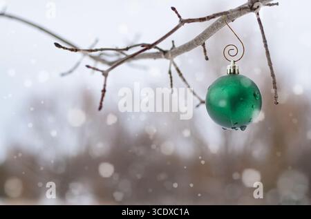 Grüner weihnachtsschmuck hängt im Winter bei Schneefall an einem Zweig im Freien Stockfoto