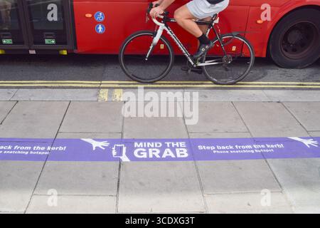 London, Großbritannien. August 2025. Ein Radfahrer kommt an einem „Mind the Grab“-Schild auf dem Bürgersteig in der Oxford Street vorbei, das einen „Hotspot“ für Telefonschnappen markiert und die Leute dazu drängt, nicht in der Nähe des Bordsteines zu laufen, um zu vermeiden, dass ihre Telefone gestohlen werden. Telefondiebstähle auf den Straßen Londons haben in den letzten Jahren zugenommen. Quelle: Vuk Valcic/Alamy Live News Stockfoto