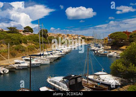 Segelboote und Yachten legen im malerischen Hafen von Stintino, Sardinien, an, umgeben von farbenfrohen Häusern und üppiger mediterraner Vegetation. Stockfoto