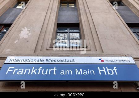 Frankfurt am Main Hauptbahnhof Eingang mit Beschilderung zur Messe Frankfurt 14.08.25, Frankfurt: Symbolfoto, Illustrationsbild, Symbolbild, Illustrationsfoto, Alltagsszene das Bild zeigt einen Teil der Fassade des Frankfurter Hauptbahnhofs mit einem blauen Hinweisschild Frankfurt am Main Hbf. Darüber befindet sich ein weiteres Schild mit dem Text Internationale Messestadt und dem Logo von Messe Frankfurt. Die Fassade wirkt verwittert und weist Putzschäden auf, was dem Bild einen urbanen-authentischen Charakter verleiht. Im oberen Bereich spiegeln sich Strukturen der Bahnhofshalle in einem Fenst Stockfoto