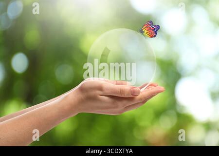 Schmetterling sitzt auf Kristallkugel in den Händen der Frau vor verschwommenem grünem Hintergrund, Nahaufnahme Stockfoto