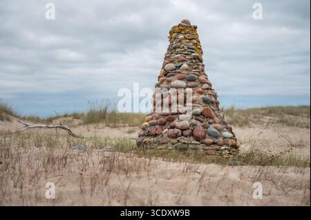 Auf einer grasbewachsenen Sanddüne steht ein einzigartiger und rustikaler Steinkairn, der aus verschiedenen runden und bunten Steinen gebaut wurde. Stockfoto