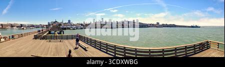 Ein malerischer Panoramablick mit einem belebten Stadthorizont am Wasser, einem Holzpier und einem klaren Himmel. Stockfoto