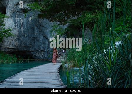 Frau überquert oder geht auf einer hölzernen Fußbrücke über den Fluss der Plitvicer Seen mit Kaskaden im Nationalpark, Kroatien, Europa. Stockfoto