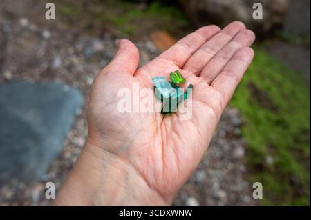 Eine detaillierte Nahaufnahme der offenen Palme einer Person mit mehreren kleinen, polierten Glasstücken. Stockfoto