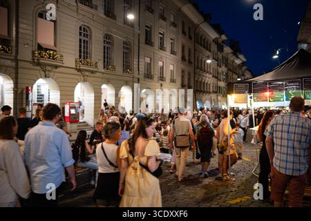 07-08-2025 Bern, Schweiz. Menschenmassen genießen das Street Food und die Aufführungen des Straßenmusikfestivals Buskers am Abend. Blaue Stundenanzeige, l Stockfoto