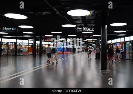 07-08-2025 Bern, Schweiz. Personen oder Pendler, die durch die unterirdische Durchgangshalle an der Hauptstation gehen. Weitwinkelansicht, Geschäfte auf beiden Seiten Stockfoto