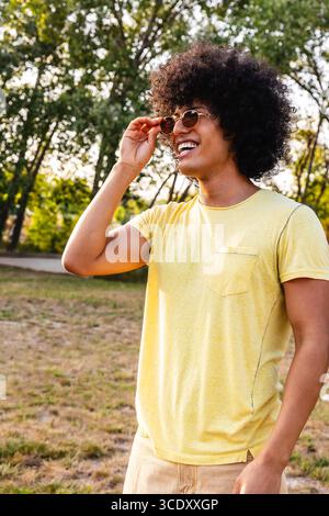 Ein junger Mann mit Sonnenbrille und einem Lächeln im Park Stockfoto