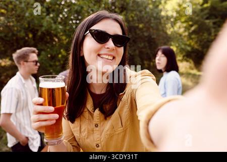 Eine junge Frau mit Bier, die Selfie auf einer Party im Freien macht Stockfoto