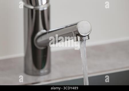 Wasser fließt aus einem modernen Chrom-Wasserhahn in ein Küchenbecken Stockfoto